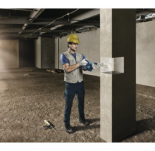 Un artisan avec un casque de protection utilise un pistolet à cartouche sans fil pour des travaux de jointoiement sur un pilier en béton.
