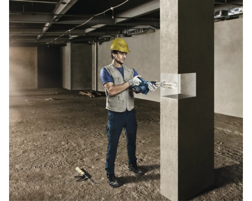 Un artisan avec un casque de protection utilise un pistolet à cartouche sans fil pour des travaux de jointoiement sur un pilier en béton.