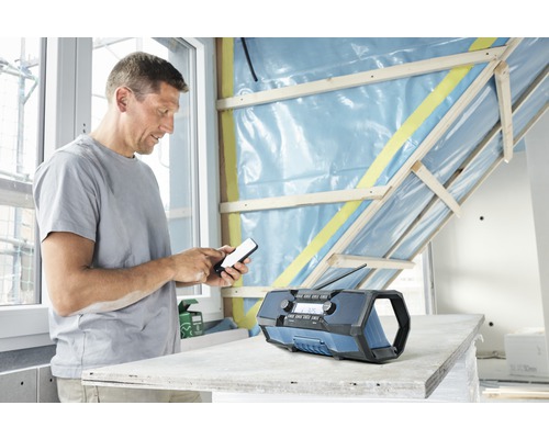 Handwerker bedient Handy neben einem Baustellenradio.