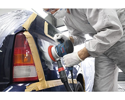 Un ouvrier ponce une voiture avec une ponceuse dans un atelier.