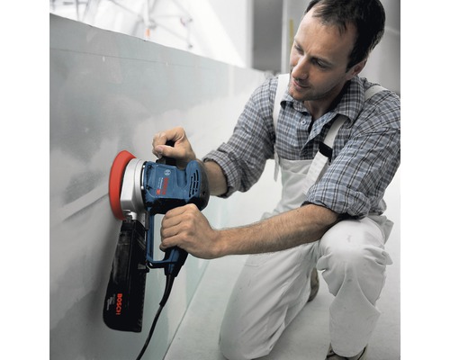 Un homme ponce un mur avec une ponceuse à plaques de plâtre Bosch