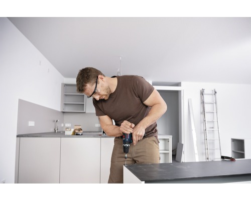 Homme avec lunettes de protection travaille avec une perceuse sans fil dans la cuisine