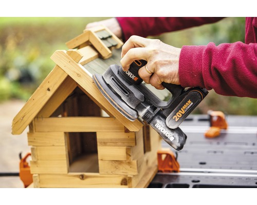 Une personne ponce une maison pour oiseaux avec une ponceuse excentrique de Worx.