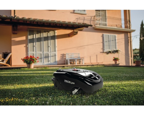 Schwarzer Rasenmähroboter der Marke Tech L20 auf einer Rasenfläche vor einem Wohnhaus.