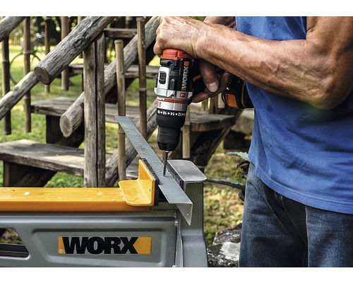 Une personne perce un trou dans une pièce métallique posée sur un établi à l''aide d''une perceuse-visseuse sans fil.