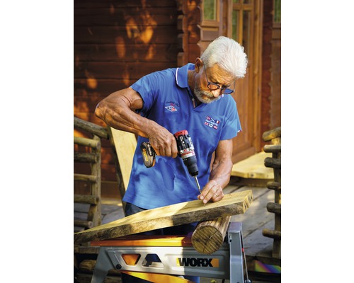 Un homme visse une planche de bois avec une perceuse sans fil, placée sur un établi.