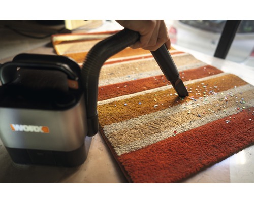 Un aspirateur sans fil est utilisé sur un tapis rayé pour enlever de petites particules. Logo de l''entreprise Worx.