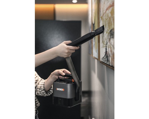 Une personne nettoie un tableau au mur avec un aspirateur portable Worx.