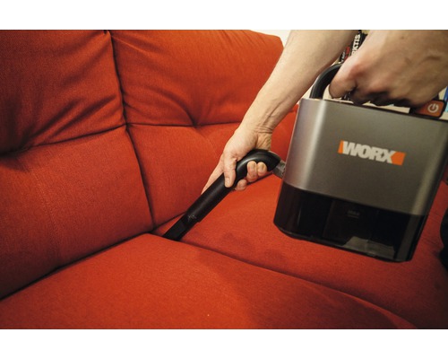 Une personne aspire un canapé avec un aspirateur sans fil Worx