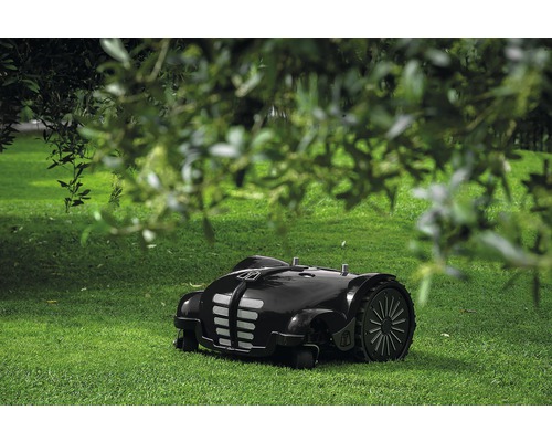 Une tondeuse robot noire se trouve sur une pelouse verte.