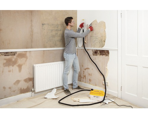 Ein Mann entfernt Tapeten mit einem Tapetenablöser in einem Raum.