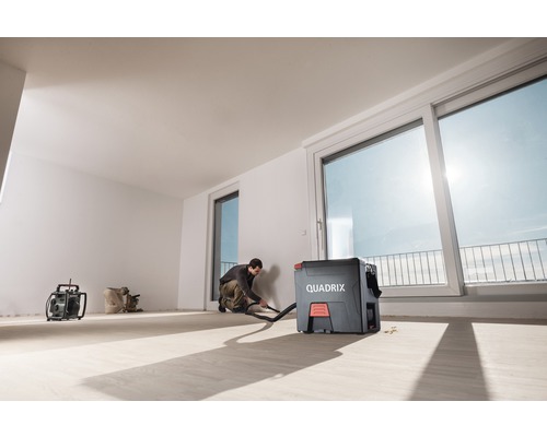 Un homme utilise un aspirateur industriel dans une pièce lumineuse avec de grandes fenêtres.