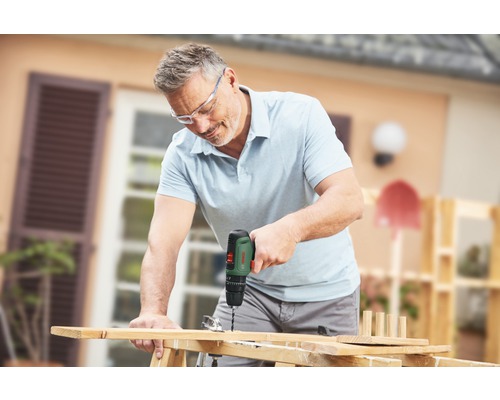 Un homme perce une planche de bois avec une perceuse tout en portant des lunettes de sécurité