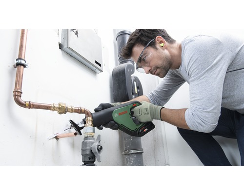 Un homme scie un tuyau de cuivre avec une scie sabre Bosch