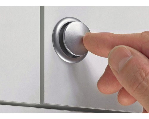 Ein Finger drückt einen silberfarbenen Möbelknopf an einer weißen Oberfläche