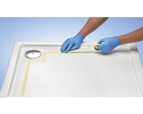 Application de ruban de masquage sur un receveur de douche en préparation de travaux d''étanchéité.