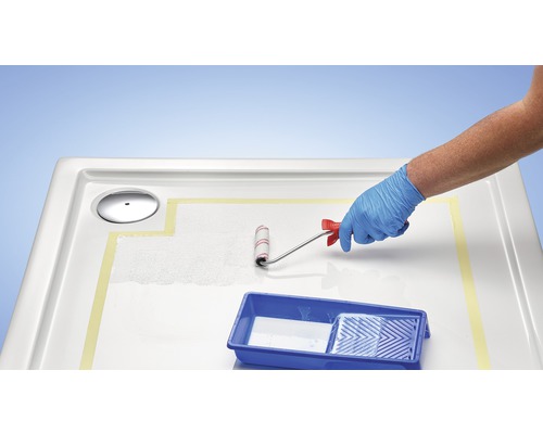 Une personne porte un gant de protection et peint un receveur de douche avec un rouleau à peinture.