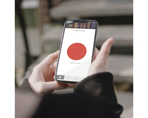 Eine Person hält ein Smartphone, das anzeigt, dass die Haustür geschlossen und verriegelt ist.