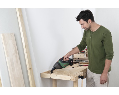 Un homme aspire un établi en bois avec un aspirateur à main sans fil.