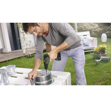 Un homme perce un trou dans un pot en métal avec une perceuse sans fil dans le jardin.