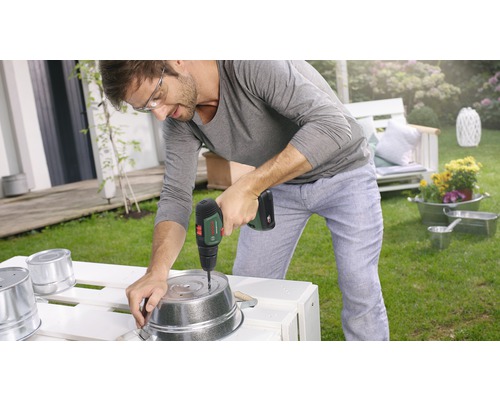 Un homme perce un trou dans un pot en métal avec une perceuse sans fil dans le jardin.