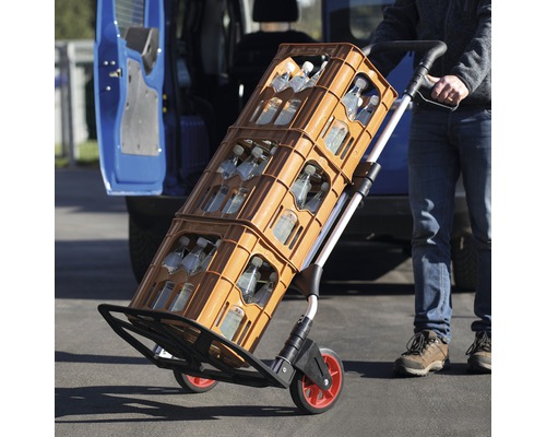 Un diable transporte des caisses de boissons devant un véhicule.