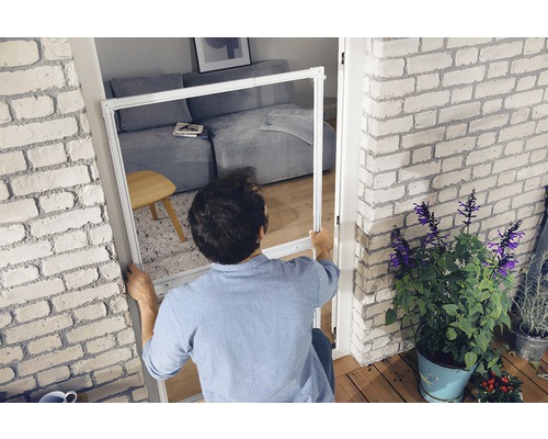 Un homme installe une moustiquaire sur un cadre de porte dans un appartement lumineux