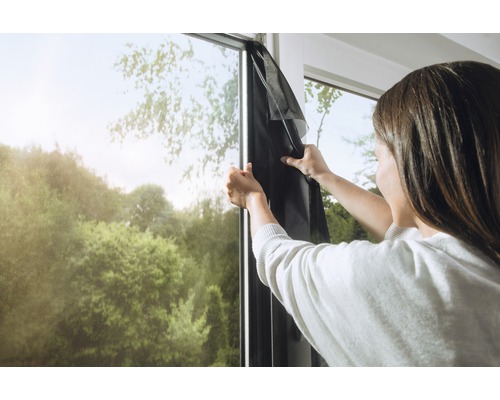 Frau befestigt Insektenschutzgitter am Fensterrahmen