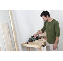 Un homme utilise un aspirateur à main sans fil sur un établi dans un atelier.