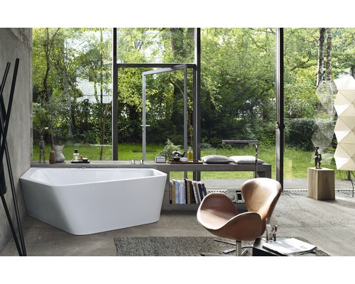 Salle de bains lumineuse avec baignoire devant une baie vitrée donnant sur le jardin, fauteuil et livres