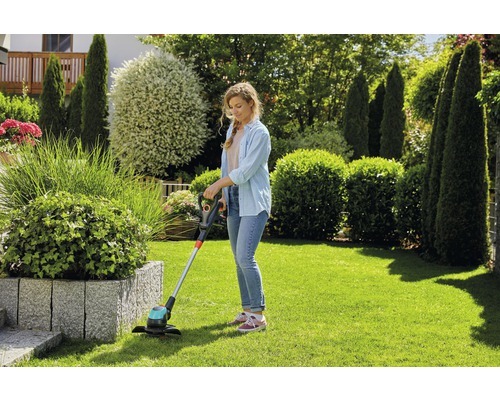 Femme coupant la pelouse avec un coupe-bordures dans le jardin.