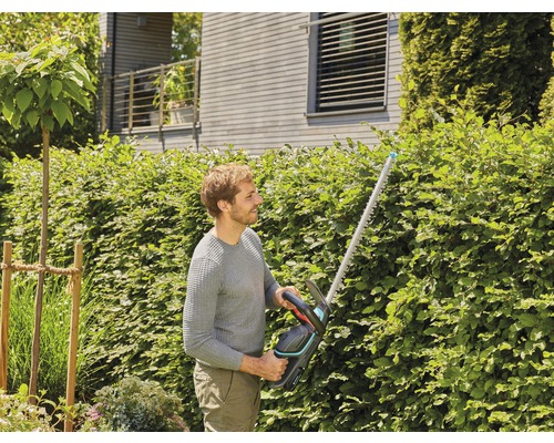 Mann schneidet Hecke mit einer Heckenschere im Garten.