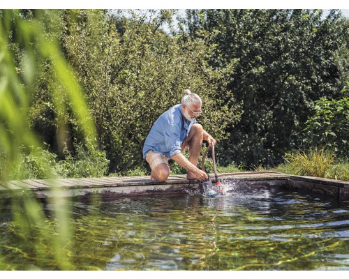 Un homme nettoie un bassin avec une brosse de bassin pour enlever les algues et la saleté.