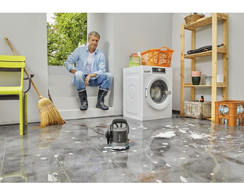 Cave inondée avec un homme assis, un lave-linge, une étagère et une pompe Gardena