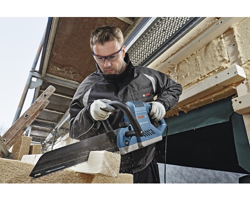 Un homme scie du bois avec une scie électrique sur un chantier de construction.