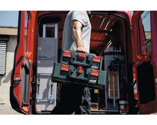 Une personne porte deux boîtes à outils Metabo devant un véhicule utilitaire.