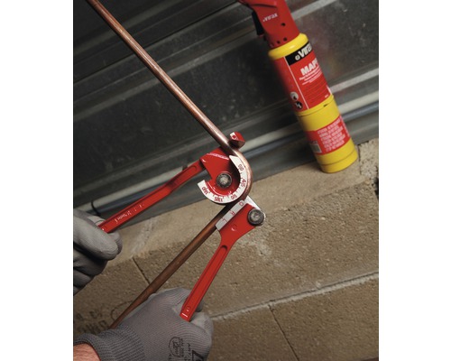 Cintreuse de tubes en action pour cintrer un tube de cuivre avec une lampe à souder en arrière-plan