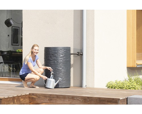 Femme remplissant un arrosoir à un récupérateur d''eau de pluie gris dans le jardin