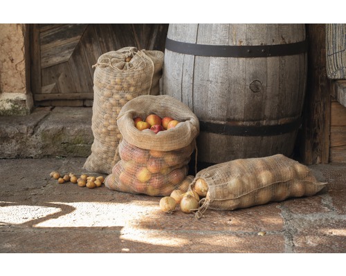 Divers sacs contenant des pommes, des pommes de terre et des oignons à côté d''un tonneau en bois