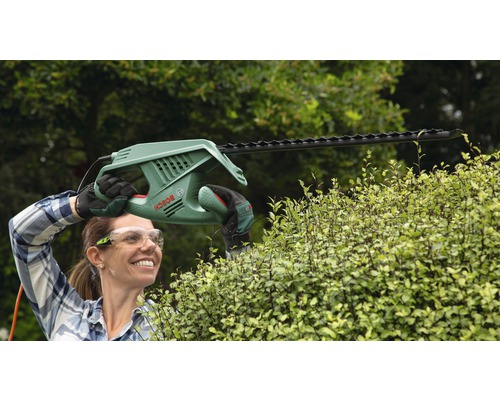 Frau schneidet Hecke mit einer elektrischen Heckenschere der Marke Bosch.