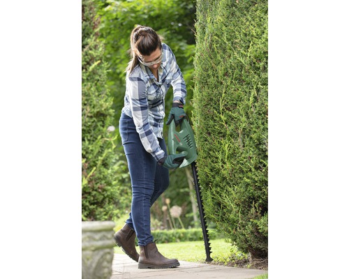 Frau schneidet Hecke mit Heckenschere von Bosch im Garten.