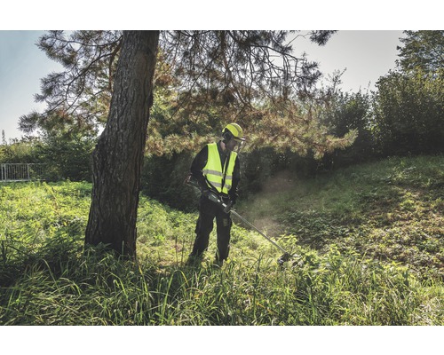 Ein Mann in Schutzkleidung arbeitet mit einem Rasentrimmer im Freien.