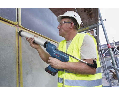 Un artisan utilise un pistolet à cartouche sans fil pour sceller un mur sur un chantier.
