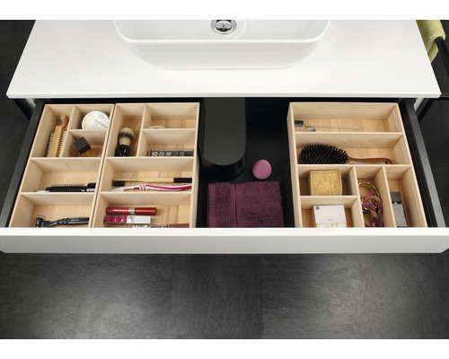 Offene Schublade eines Waschtischunterschranks mit Holzfächern und diversen Badartikeln