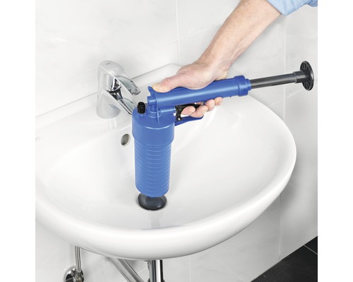Hand betätigt eine blaue Rohrreinigungs-Pistole über einem Waschbecken, um eine Verstopfung zu lösen.
