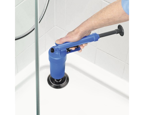 Eine Hand benutzt einen blauen Saugstempel mit Griff in einer Dusche, um einen Abfluss zu reinigen.