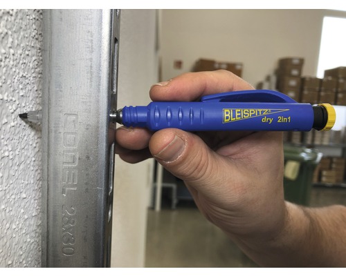 Une main marque un mur au crayon à travers un profilé métallique