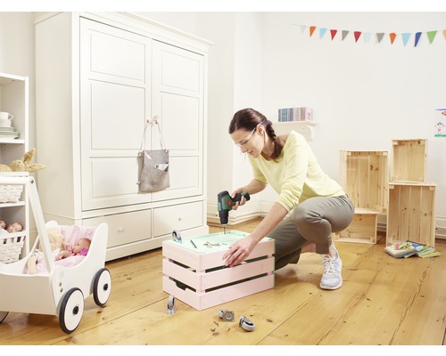 Une femme travaille avec une visseuse sans fil sur une caisse dans une chambre d''enfant avec une poussette et une armoire