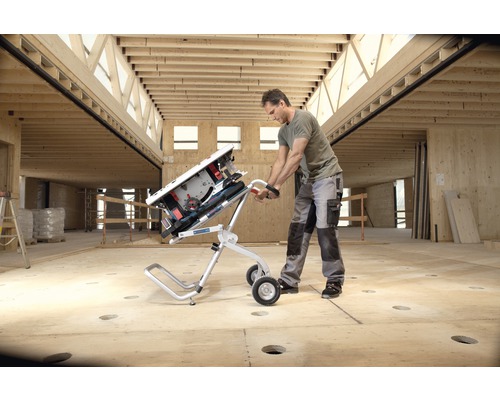 Mann transportiert Tischkreissäge mit Transportwagen in Rohbau