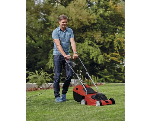 Mann mäht Rasen mit einem roten Elektrorasenmäher im Garten.